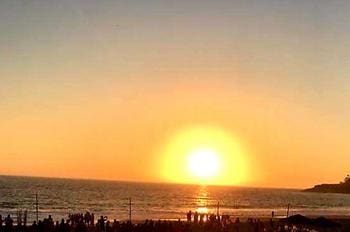 A sunset over the ocean with people standing on it.