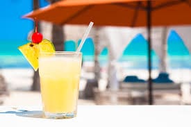 A glass of juice on the beach with an umbrella in the background.