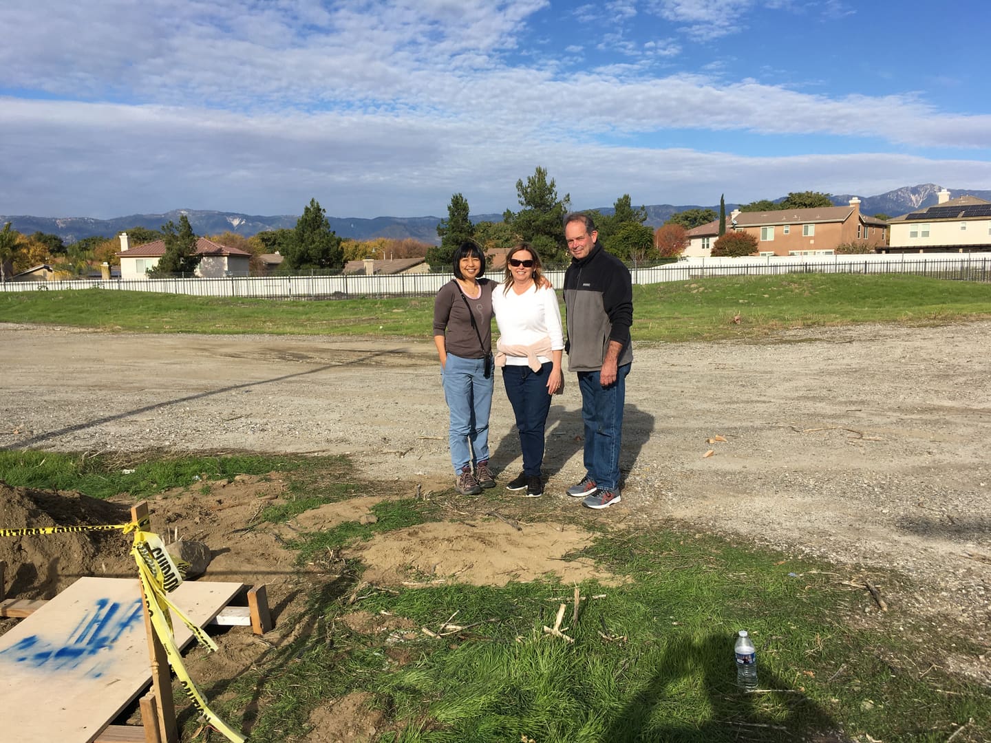 Three people standing in a field with a building behind them.