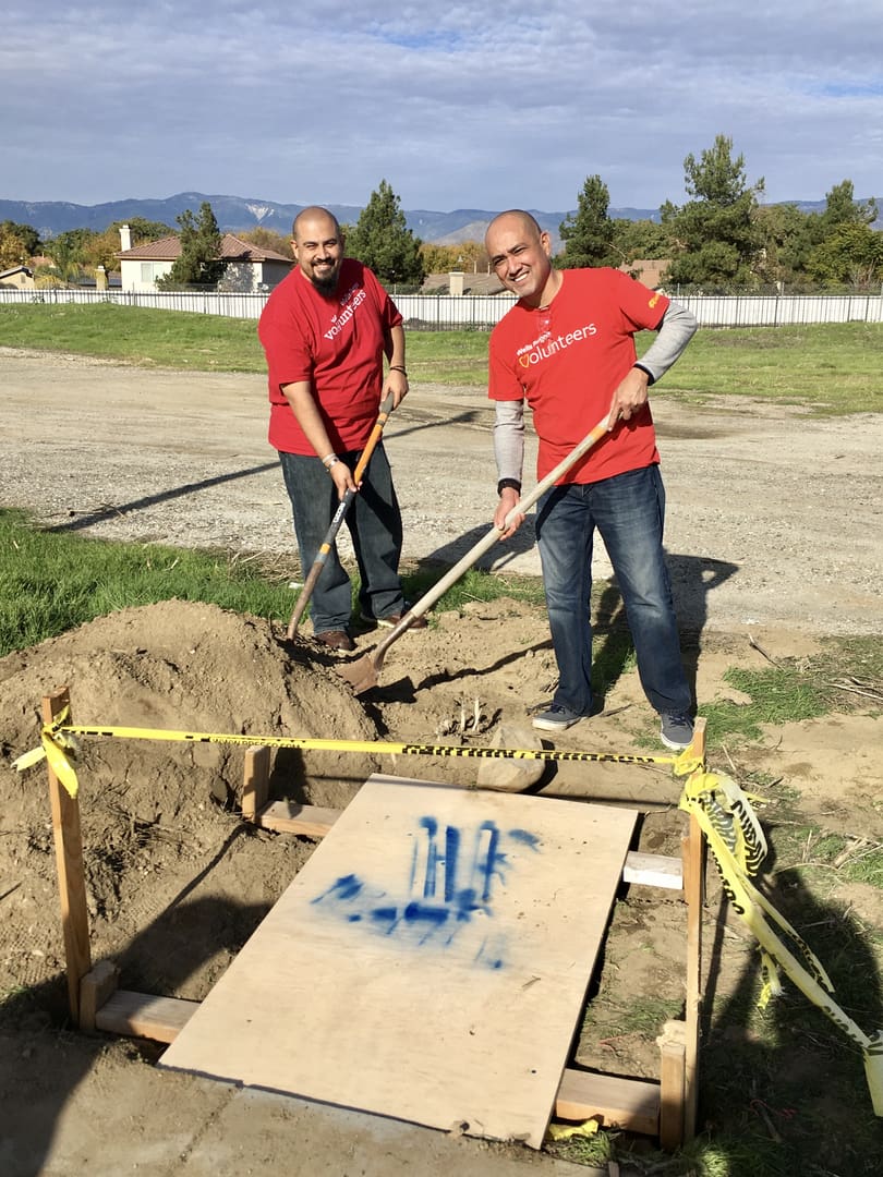 Two men in red shirts are digging a hole.