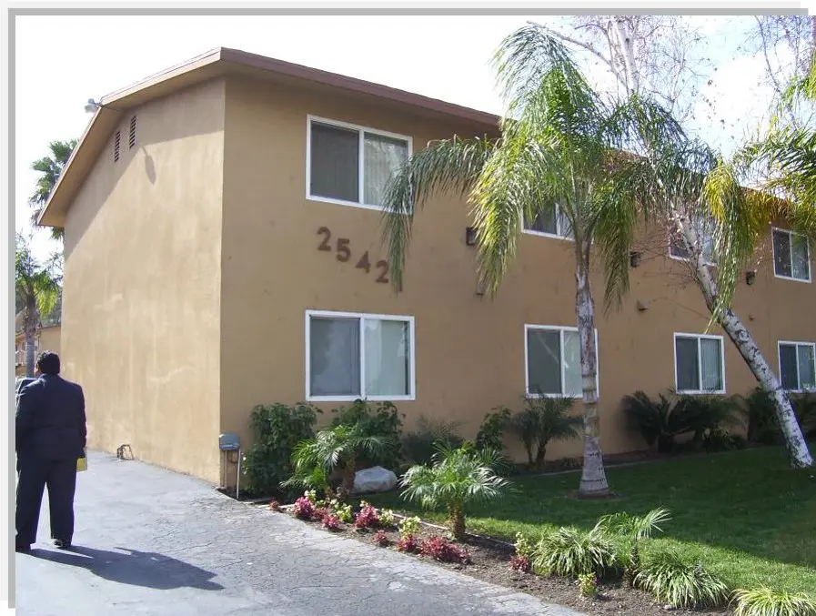 A tan building with palm trees and bushes in front of it.