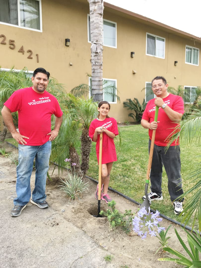 Three people in red shirts are standing outside