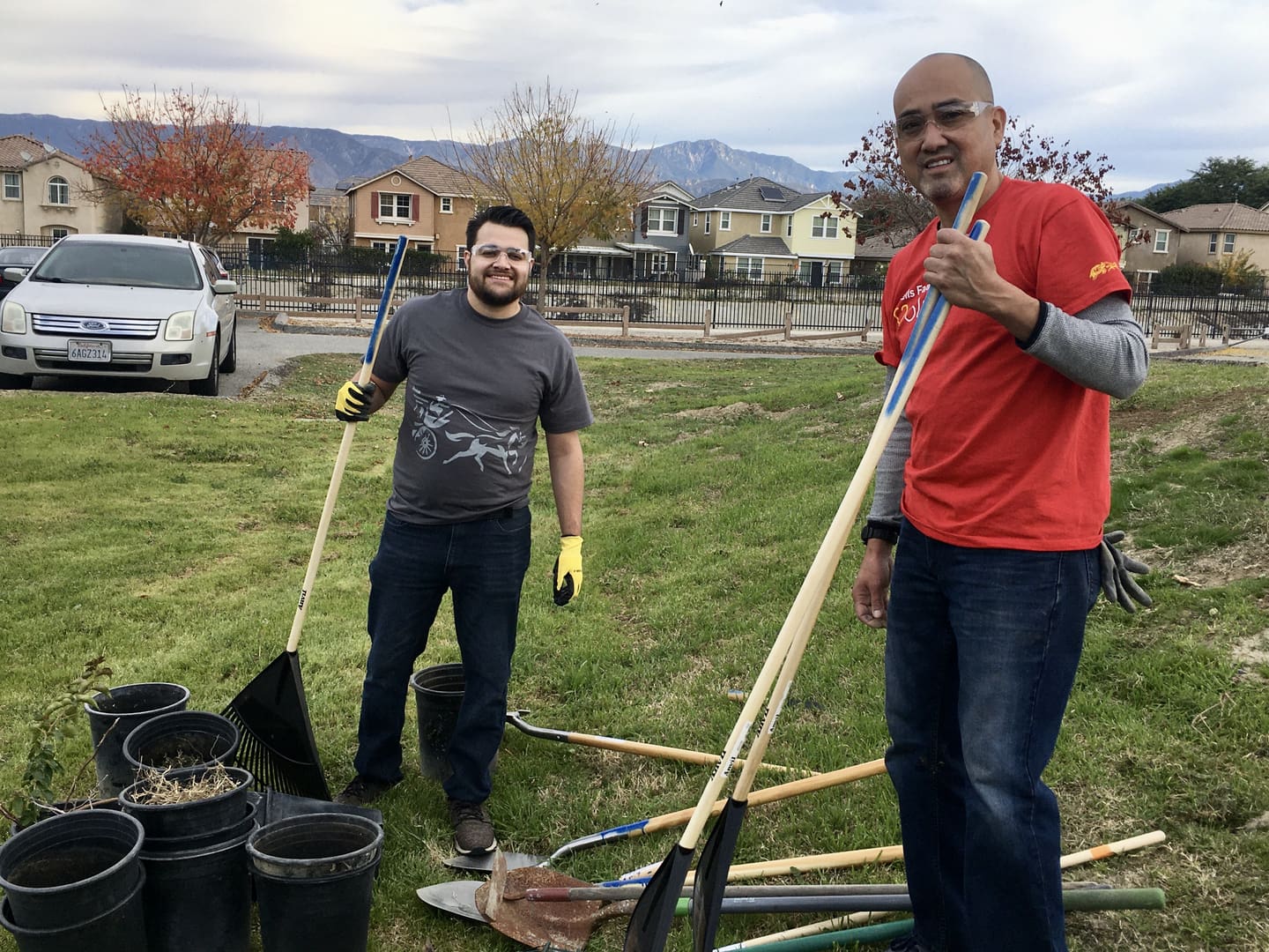 Two men are standing in a field with shovels.