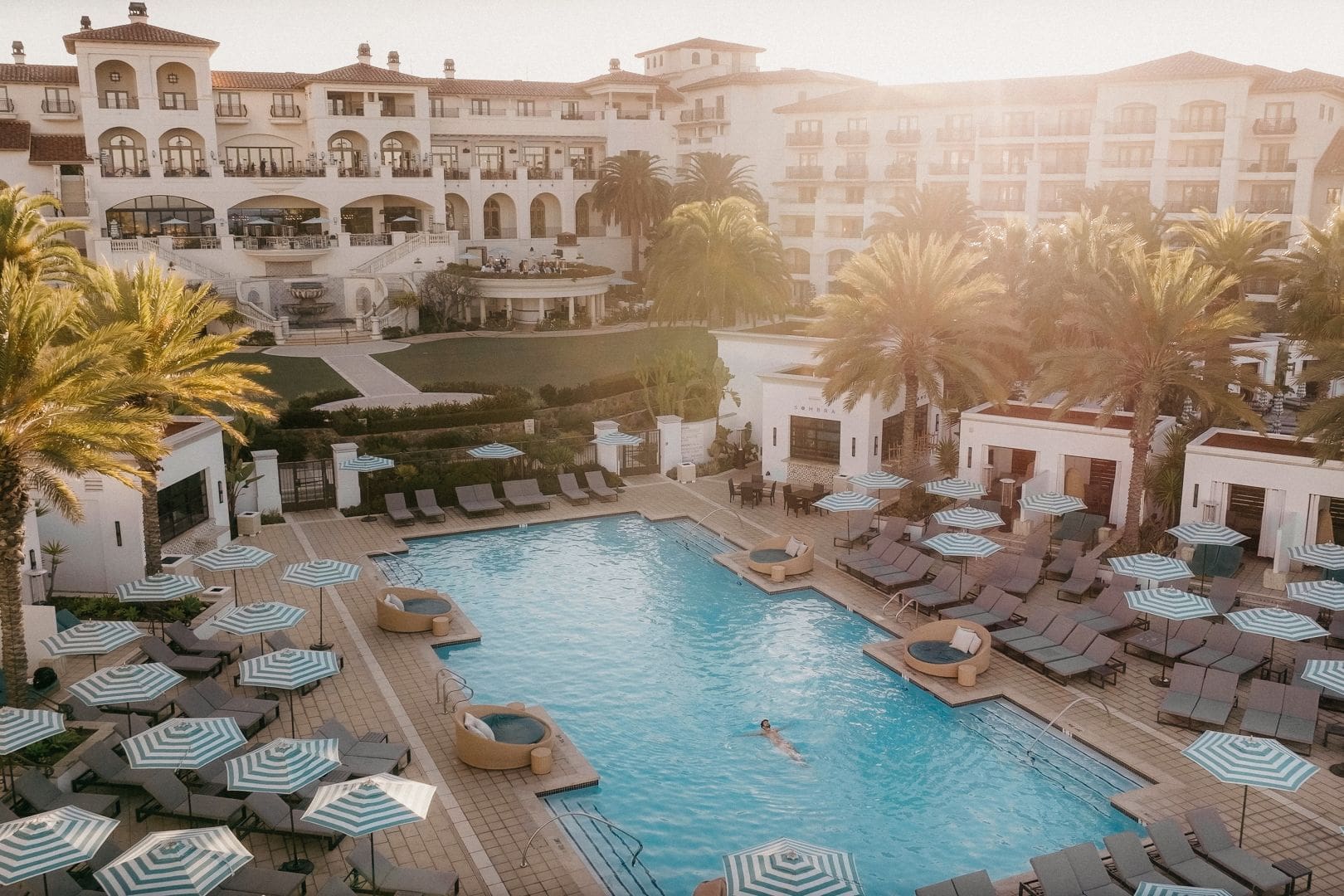 A pool with many chairs and umbrellas in the sun.